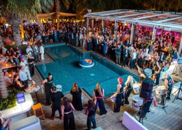people from maritime industry standing at columbia beach restaurant surrounding a pool to watch drummers play at a cocktail party